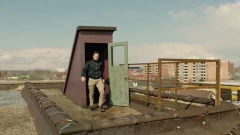 Angry Caucasian man aggressively walks out of a door to a rooftop to a warehouse Stock Footage 199461663