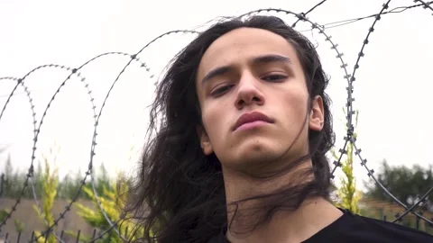 Angry long haired cool young protest man standing staring in front of wire ne Stock Footage 160195063