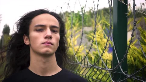Angry long haired youth protestor man standing staring in front of wire netti Stock Footage 160195346
