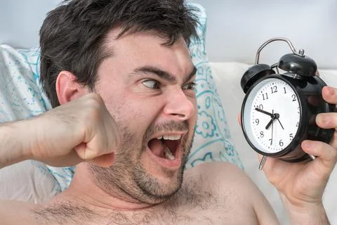 Angry man with alarm clock does not want waking up and go to work Foto stock