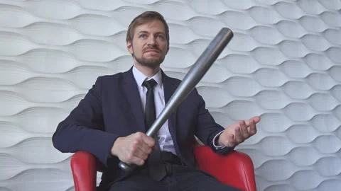 Angry man with a baseball bat sitting on a red chair Stock Footage 130869662
