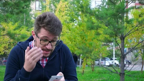 Angry man with a beard sitting in the Park. Writes messages in phone Stockbeeldmateriaal 95161066