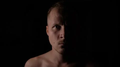 Angry man in the dark. Only half of the face is highlighted. Stock Photos