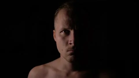 Angry man in the dark. Only half of the face is highlighted. Stock Photos
