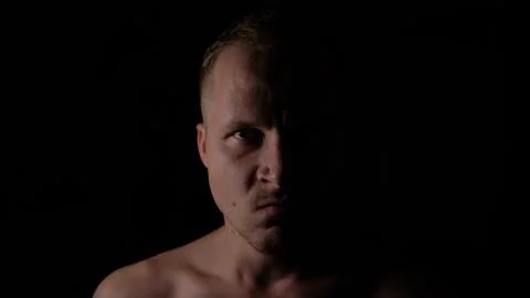Angry man in the dark. Only half of the face is highlighted. Stock Photos
