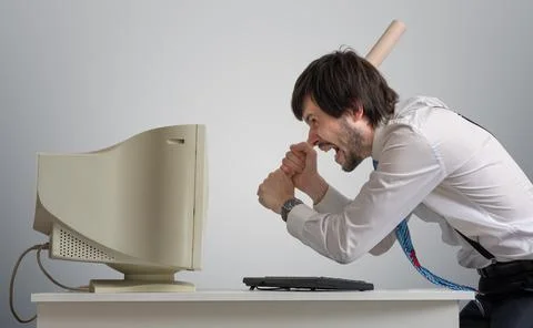 Angry man is destroying old computer with baseball bat in office. Stock Photos