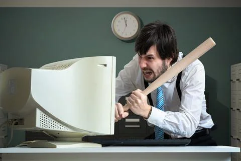 Angry man is destroying old computer with baseball bat in office. Stock Photos