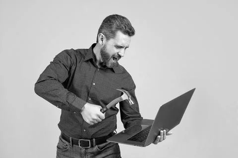 Angry man hit laptop computer with hammer grey background, crash Stock Photos