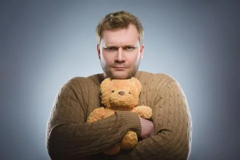 Angry man is holding a teddy bear and smiling on gray background Stock Photos