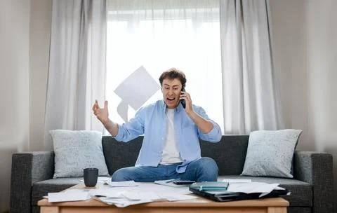 Angry man on phone throws overdue utility bills in despair. He faces severe.. Stock Photos