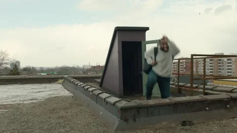 Angry man runs out through a door to a warehouse rooftop, catches his breath and Stock Footage 199459777