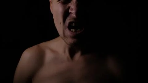 Angry man. A screaming evil expression. Close-up of the man's face in the dark. Stock Photos
