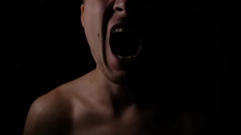Angry man. A screaming evil expression. Close-up of the man's face in the dark. Stock Photos