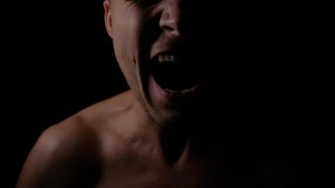 Angry man. A screaming evil expression. Close-up of the man's face in the dark. Stock Photos