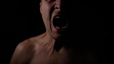 Angry man. A screaming evil expression. Close-up of the man's face in the dark. Stock Photos
