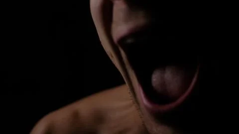 Angry man. A screaming evil expression. Close-up of the man's face in the dark. Stock Photos