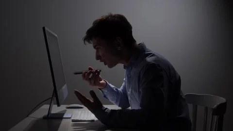 Angry man sitting in dark office yelling into a mobile phone, experiencing Stock Footage 342672048