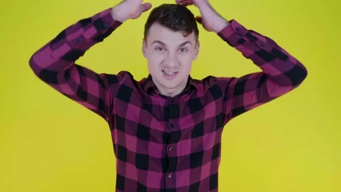 An angry man takes head in hands and shouts at the camera on a yellow background Stock Footage 132449745