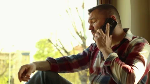 Angry man talking on cellphone, sitting near window Stock Footage 62824200