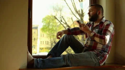 Angry man talking on cellphone, sitting on windowsill Stock Footage 62824308