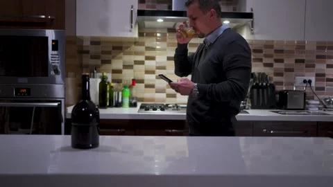 Angry Man Talking on Smartphone and Drinking Whiskey in Kitchen. A man look.. Video stock 332416055