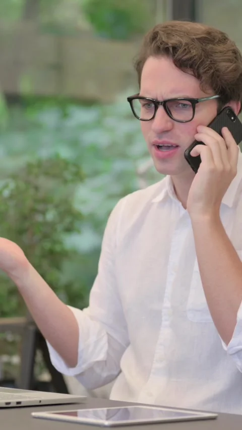 Angry Man Talking on Smartphone while Using Laptop in Modern Office, Vertical Stock Footage 340032327