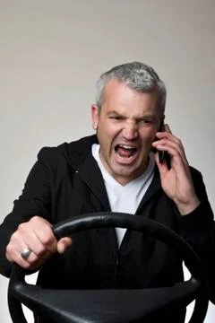 An angry man using a mobile phone behind a car steering wheel Stock Photos