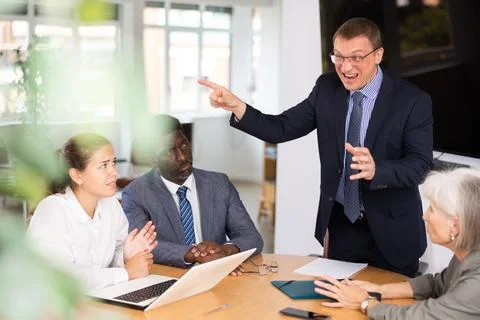 Angry middle-aged man shouting at his business partners sitting around table Stock Photos