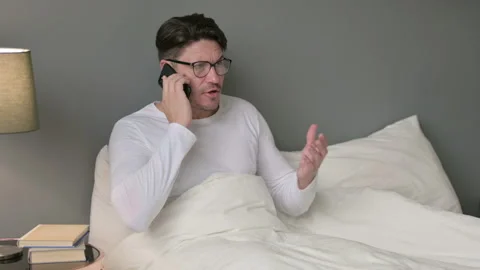 Angry Middle Aged Man Talking on Smartphone in Bed 스톡 동영상 142380373