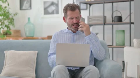 Angry Middle Aged Man Talking on Phone with Laptop in Lap Stock Footage 287898384