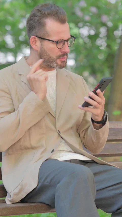 Angry Middle Aged Man Talking on Phone in Argument while Sitting Outdoor on Video stock 319012516