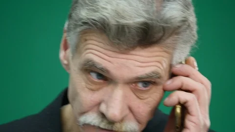 Angry senior man speaking on mobile phone on green background Stock Footage 86169027
