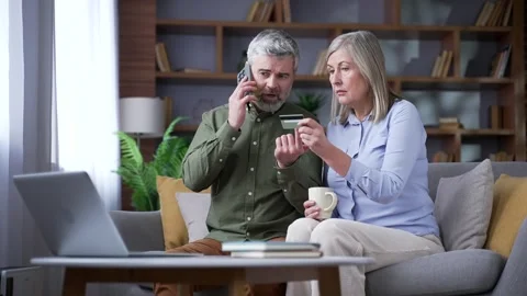 Angry senior man talking on a smartphone while sitting on a sofa beside his wife Stock Footage 339775695