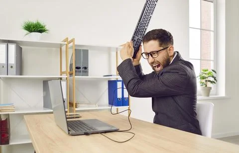 Angry shouting man working on workplace in office trying to destroy the monitor Stock Photos