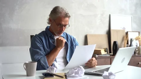 Angry stressed middle-aged man with laptop and papers working at home office Stock Footage 141192417