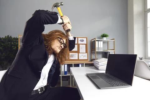 Angry stressed office worker hitting laptop computer with hammer on bad day at Stock Photos