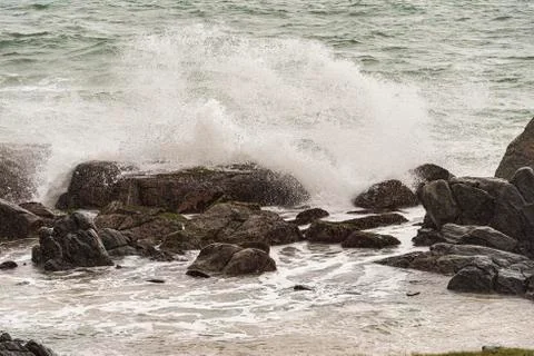 Angry waves crash over rocks on the coast during a summer storm Stock Photos