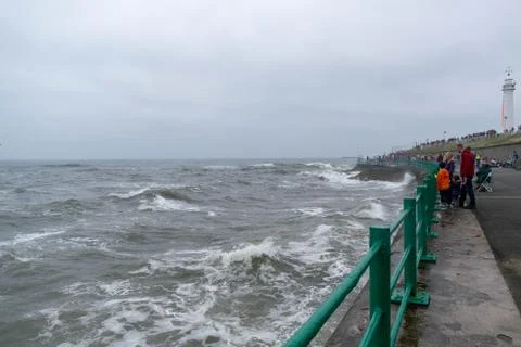 Angry waves roll and splash in the ocean whilst families watch Stockfoto's