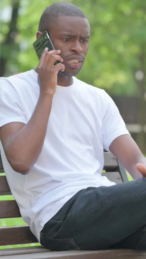 Angry Young African Man Talking on Phone while Sitting Outdoor on Bench, Video stock 319021911