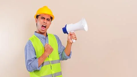 Angry young asian construction worker man shouting through megaphone wearin.. Stock Photos
