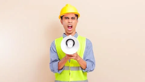 Angry young asian construction worker man shouting through megaphone wearin.. Stock Photos
