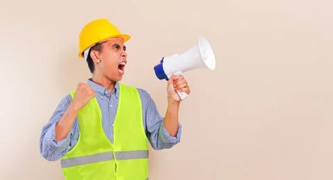 Angry young asian construction worker man shouting through megaphone wearin.. Stock Photos