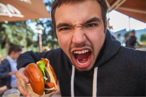 Angry young man looking at the camera with his mouth wide open. He is holding Stock Photos