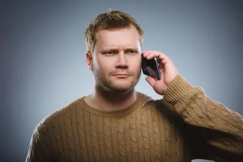 Angry young man talking on cell phone isolated on gray background Stock Photos