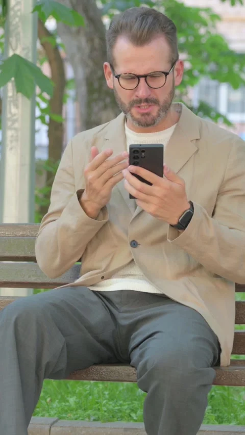 Angry Young Man Talking on Phone in Argument while Sitting Outdoor, Vertical Stock-Footage 319018602