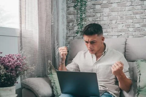 Angry young man using computer pc at home sitting on the sofa having problems Stock Photos