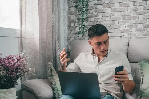 Angry young man using computer pc at home sitting on the sofa having problems 库存照片