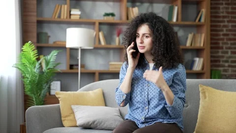 Angry young woman arguing while talking on the phone sitting on the sofa  Stock Footage 320414695