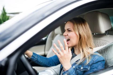 Angry young woman driver sitting in car, shouting. Stock Photos