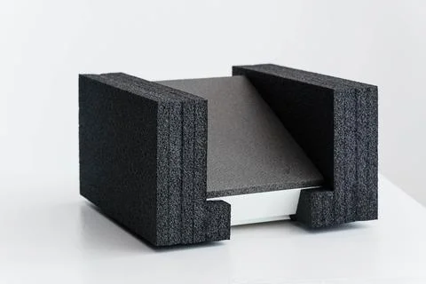 Angular Gray Object Resting Between Two Textured Black Foam Supports on Whi.. Stock Photos